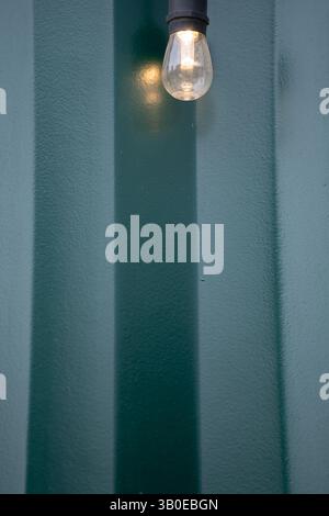 Vertical image of electric light bulb lit light is shining and reflecting off of wet wall exterior edison light glass bulb idea background backdrop Stock Photo