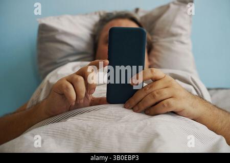 Relaxing in Bed While Using Smartphone Device Stock Photo