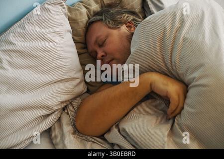 Sleeping Man Resting Peacefully on Striped Bedding Stock Photo