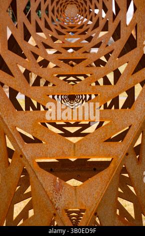 close up vertical of an intricately cut outdoor rusty oxidized metal sculpture of geometrical shapes with depth into infinity and shadows symmetrical Stock Photo