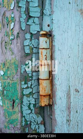rusty old door hinge painted turquoise with peeled paint on hinge and door creating a grungy feel vertical image with abstract shapes of peeling paint Stock Photo