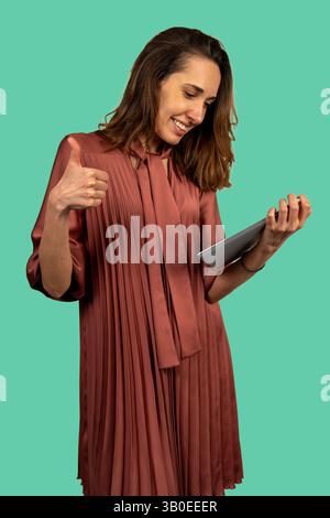 Happy businesswoman showing thumb up while using a tablet, isolated on a turquoise background Stock Photo