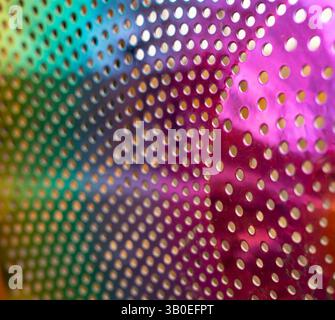 close up of pink and green metal cylinder with multiple holes reflecting metal colored pink and green and reflecting light rings of tiny holes in flow Stock Photo