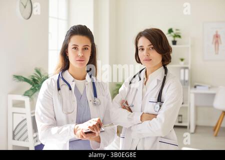 Two confident female doctors with stethoscopes standing in medical office and looking at camera. Stock Photo