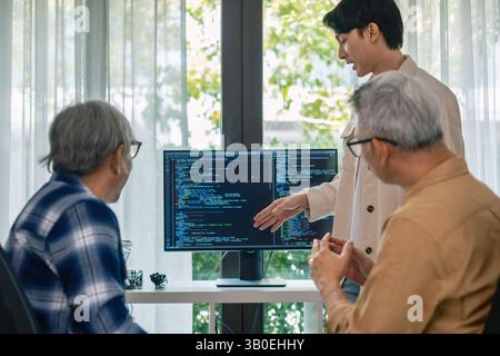 senior programmer bootcamlp,Asian young instructor guides senior learners through a programming on whiteboard, highlighting algorithm thinking and sim Stock Photo