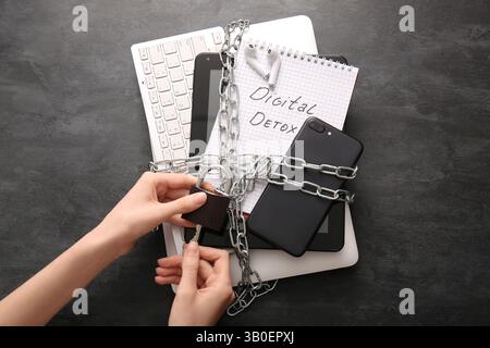 Woman closing padlock with chain on gadgets against dark background, closeup Stock Photo
