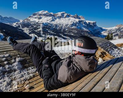 Boy Relaxing on Wooden Bench in Snowy Mountains - Outdoor Winter Relaxation in Alpine Scenery. Stock Photo