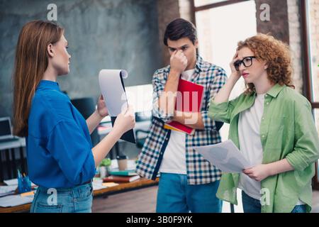 Three coworkers engaged in a conversation at a bright office discussing project details in a group meeting setting Stock Photo
