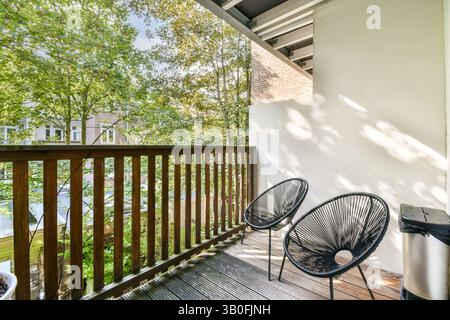 A serene balcony scene featuring two stylish chairs amidst lush green trees, providing a peaceful outdoor retreat in a modern setting. Stock Photo