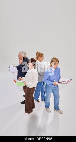 View from above on four elderly people, students involved in learning session, standing with books, studying against white background. Stock Photo