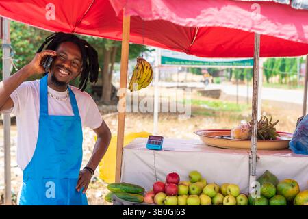 African american trader in a market space making use of mobile phone. excited businessman on dreads lock using smartphone, connecting to internet. Tec Stock Photo