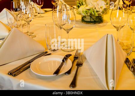 A beautifully set dining table with elegant white napkins, glassware, and cutlery arranged neatly. The centerpiece features fresh flowers, creating a Stock Photo