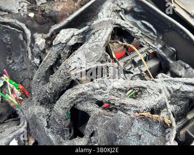 Burned car fuse box and wiring with melted insulation, scorched plastic housing, and exposed colored wires after extensive fire damage in the engine c Stock Photo