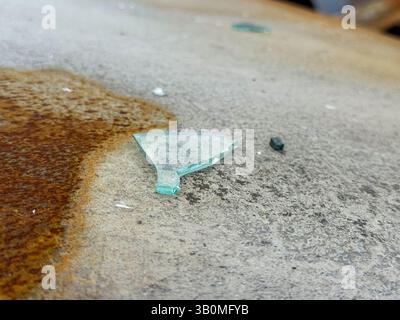 Shard of broken automotive glass on the rusted and scorched roof of a burned car, showing detail of the surface texture and remnants of fire damage. Stock Photo