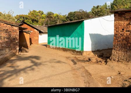 One new house in vivid colours surrounded with old brick houses in a small village in rural Orissa in India Stock Photo