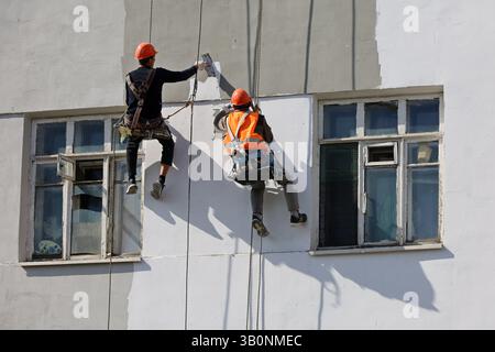 Workers repair the building wall while hanging on safety ropes. Builders painting of the house facade, construction and repair works Stock Photo