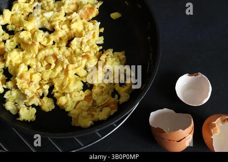 Scrambled eggs with spices and herbs in a pan on a black background. Healthy breakfast. Directly above. Stock Photo