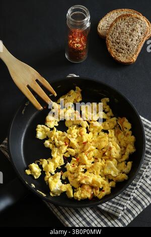 Scrambled eggs with spices and herbs in a pan on a black background. Healthy breakfast. Directly above. Stock Photo