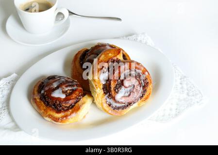 Cinnamon rolls. Roll of walnut brioche pastry, decorated with a veil of icing and cup of coffee on white wooden background.Nuss-schnecke Walnut snails. Stock Photo