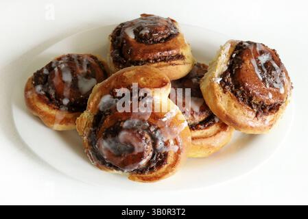 Cinnamon rolls. Fragrant roll of walnut brioche pastry, decorated with a veil of icing  on white wooden background. Nuss-schnecke (Walnut snails). Stock Photo