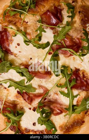 A crisp, golden pizza topped with creamy burrata, prosciutto, fresh arugula, and a sprinkle of chili flakes, captured in warm, natural light. Stock Photo