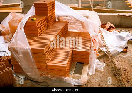 Pile of red blocks packed in open plastic foil placed on pallet to mount a wall at construction site. Stock Photo
