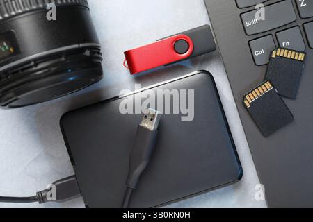 Flash drive connected to laptop, SD memory cards, external hard disk and camera lens on gray textured table, flat lay Stock Photo