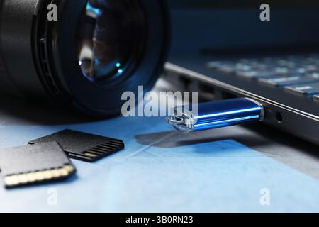 Flash drive connected to laptop, SD memory cards and camera lens on gray table, closeup Stock Photo