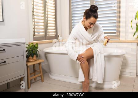 Brushing woman sitting on edge of bathtub in home bathroom, holding wooden dry brush, copy space Stock Photo