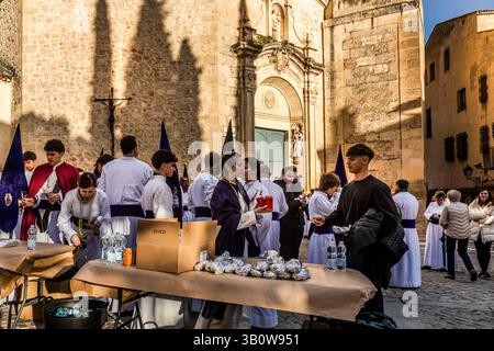 Numerous members of the Hermandad del Bautismo de Nuestro Señor Jesucristo fortify themselves before the Procesión del Perdón (Procession of Forgiveness) in front of the Iglesia de San Pedro in Cuenca, Castilla-La Mancha, Spain. Hornazo, a bread filled with ham, chorizo and egg, is the typical marching provisions of the Banceros. In Cuenca, this is the local term for what are known elsewhere in Spain as costaleros, the teams who carry the processional floats. Stock Photo