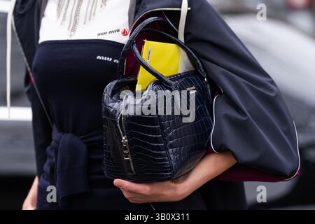 Paris, France - March 11, 2025: Woman wears Prada croc-embossed black leather handbag with gold logo and yellow folder. Fashion blogger outfit details Stock Photo