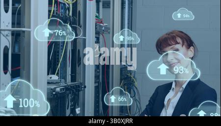 Image of cloud icons with growing numbers over caucasian woman in server room Stock Photo