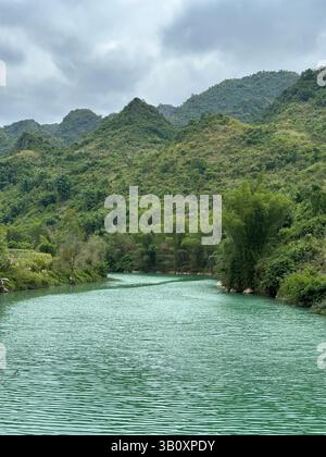 A beautiful view of a river flowing through green, mountainous terrain on a cloudy day. Stock Photo