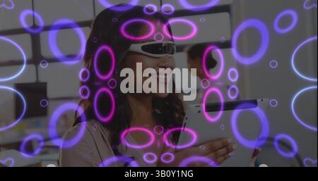 Image of neon shapes over biracial woman using vr glasses and tablet Stock Photo