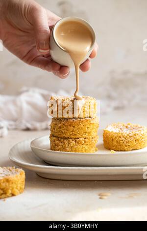 Mini almond cakes with a coffee cream sauce being poured over them Stock Photo