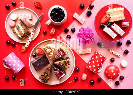 Pop art food, color blocking aesthetic with double layer cream filled assorted cakes, cherries, macarons and strawberries. Stock Photo