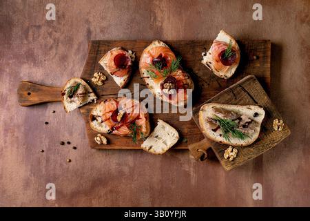 Sandwiches with thinly sliced salted salmon fillet, sardines, beetroot slices, walnuts, balsamic vinegar and fresh wheat bread on wooden board. Brown Stock Photo