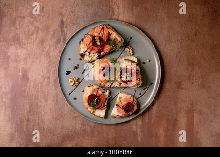 Sandwiches with thinly sliced salted salmon fillet, beetroot slices, walnuts, balsamic vinegar and fresh wheat bread on grey plate, fine dining. Brown Stock Photo