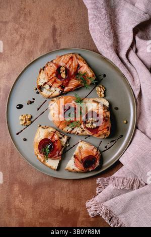 Sandwiches with thinly sliced salted salmon fillet, beetroot slices, walnuts, balsamic vinegar and fresh wheat bread on grey plate, fine dining. Brown Stock Photo