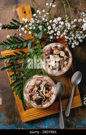 Classic Italian tiramisu layered dessert with cocoa powder and almonds in two glasses. Served on tray with spoons on old wooden table. Decorated white Stock Photo