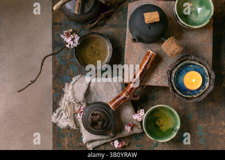 Chinese Tea Ceremony. Three traditional handmade ceramic black teapots with wooden handle on dark wooden table. Ceramic teacups and pink spring flower Stock Photo