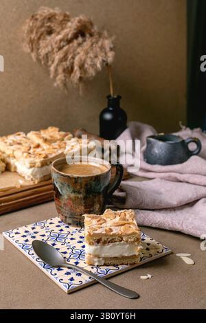 Homemade Norwegian cake Verdens Beste Kake with custard, meringue, and almonds, cut into squares, served on wooden tray. Extra piece on plate with cof Stock Photo