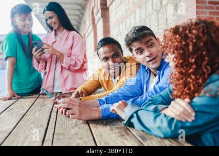 Young friends using mobile phone. Diverse students having fun with smartphones outside school university. Youth culture concept Stock Photo