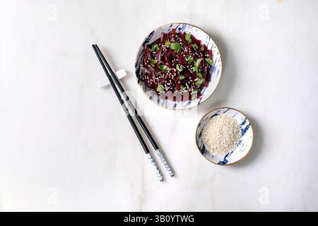 Korean-style vegan beet salad. Marinated grated beetroot with sesame seeds and coriander leaves in ceramic bowl. Nearby bowl with sesame seeds and cho Stock Photo