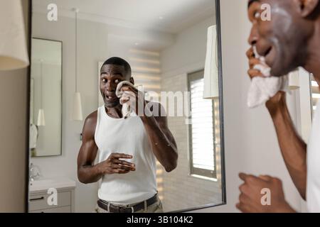 African American man dabbing face with washcloth before mirror in bathroom, with pendant light Stock Photo