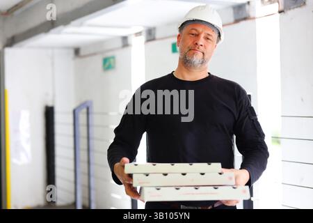Builder with lunch delivery in hands, wearing safety helmet and black uniform Stock Photo