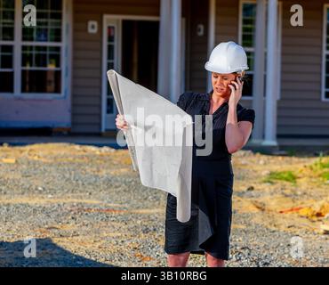 A young female construction supervisor studies house blueprints on-site, ensuring builders understand the design and construction sequence, confidentl Stock Photo