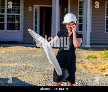 A young female construction supervisor studies house blueprints on-site, ensuring builders understand the design and construction sequence, confidentl Stock Photo