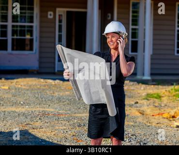 A young female construction supervisor studies house blueprints on-site, ensuring builders understand the design and construction sequence, confidentl Stock Photo