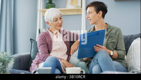 Home, senior woman and daughter with document, care and explaining benefits of policy in living room. House, elderly mother and paperwork with info Stock Photo
